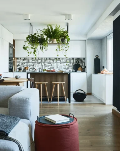 Stylish living room interior design with grey sofa, pouf and personal accessories. Dining space and kitchen on the background. Creative walls with woode pannels. Minimalistic style an plant love concept.